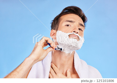 Portrait, shave and bathroom with a man model shaving his face in studio on a blue background for grooming. Beauty, skincare and shaving foam with a handsome young male using a razor in the morning 125101806