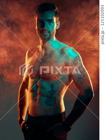 Fashion, body and smoke with a man model in studio on a gray background with red mist for contemporary style. Fitness, beauty and portrait with a topless young handsome male posing in a smokey haze 125102093