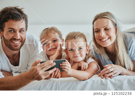 Happy, family and relax with phone on the bed in fun entertainment streaming together at home. Mother, father and children relaxing in the bedroom with smile for online shows on smartphone indoors 125102238