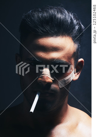 Cigarette, boxer and man with fighting injury, wound and bandaid after fight, violence or accident in a dark studio. Portrait of fighter, shadow or gangster smoking after MMA match or crime 125102468