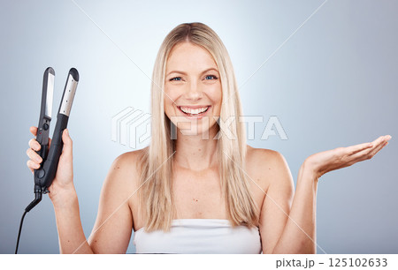 Hair care, woman and flat iron with smile, happy and natural beauty with grey studio background. Portrait, female or girl with stylish perm, content or relax with shine, salon look or fresh hairstyle 125102633