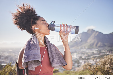 Music, workout and woman drinking water after exercise at sunrise along mountain, wellness and training on blue sky. Radio, water and black woman stop for break from fitness, running and cardio run 125102798