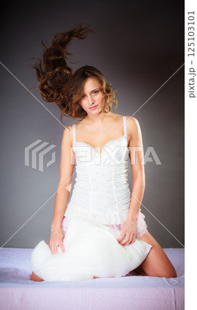 Woman on bed with pillow and wind in hair. 125103101