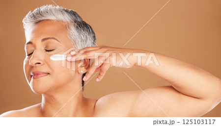 Cream, skincare and senior woman with peace, wellness and care for skin against a brown studio background. Smile, dermatology and calm elderly model with sunscreen for facial and body health Cream, skincare and senior woman with peace, wellness and care for skin against a brown studio background. Smile, dermatology and calm elderly model with sunscreen for facial and body health 125103117