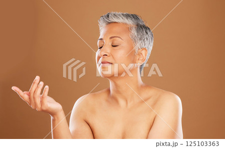 Skincare, senior woman and beauty with hand for cosmetics, makeup and dermatology product, mockup and advertising on brown studio background. Mature model posing for cosmetology, skin and wellness 125103363