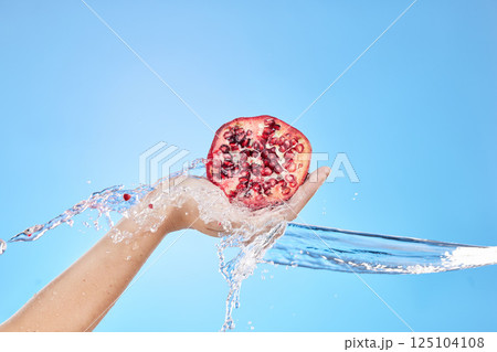 Water splash, hand and pomegranate for health in studio on blue background mockup. Fresh fruits, cleaning hygiene and female model holding fruit food for vitamin c, organic cosmetics or glowing skin. 125104108
