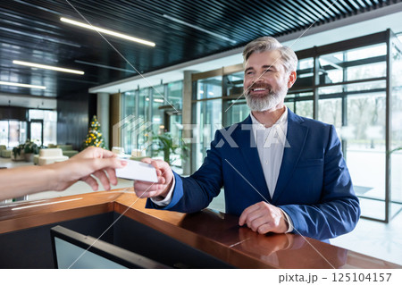 Bearded male staff at reception counter giving key card 125104157