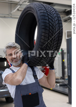 Man in service shop wearing uniform performing manual job to change tyres Man in service shop wearing uniform performing manual job to change tyres 125104334