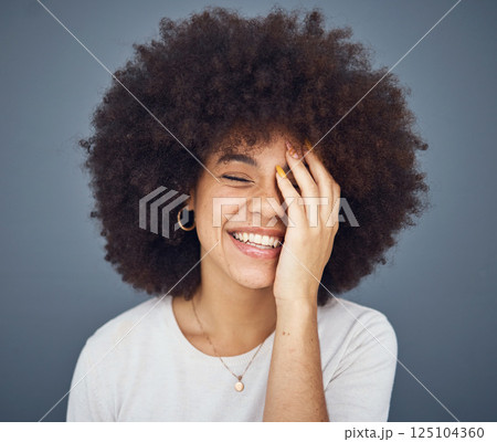 Comic, happy and black woman with a smile for memory, comedy and fashion against a grey studio background. Hair care, salon and young African girl with an afro while crazy, funny and healthy 125104360