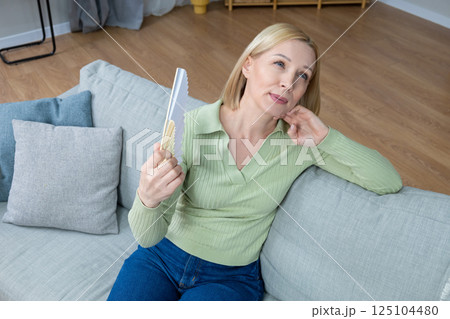 50 year old woman sitting with a fan in hand and suffering from heat 50 year old woman sitting with a fan in hand and suffering from heat 125104480