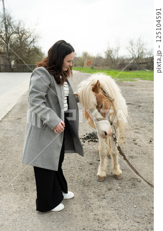 Woman stroking pet cute pony, friendship of people and animals 125104591