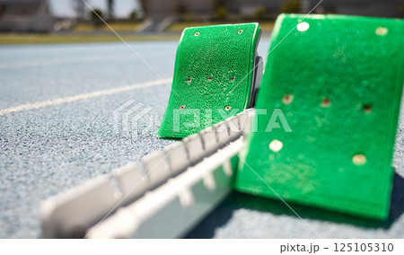 Sports closeup, starting blocks and running track, field or pitch for training, exercise or sprint in arena. Start, ready and race with equipment for sport, fitness or workout on ground at stadium Sports closeup, starting blocks and running track, field or pitch for training, exercise or sprint in arena. Start, ready and race with equipment for sport, fitness or workout on ground at stadium 125105310