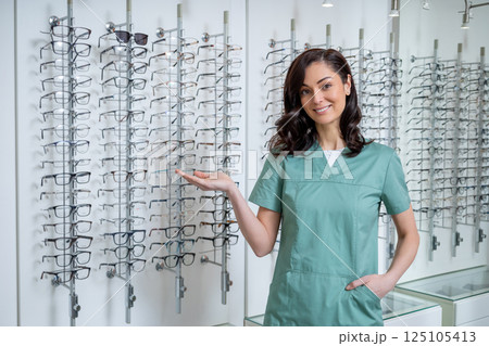 Young female ophthalmologist standing near glasses stand and demonstrating new models Young female ophthalmologist standing near glasses stand and demonstrating new models 125105413