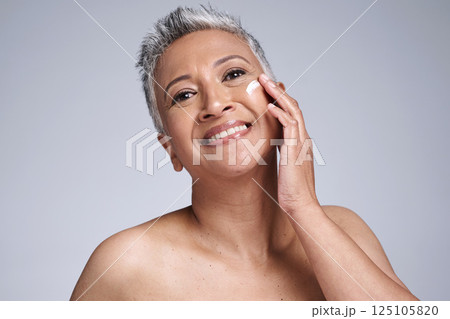 Face, skincare and beauty with a mature woman using moisturizer for antiaging treatment in studio on a gray background. Wellness, facial and portrait with a senior female inside for dermatology care 125105820