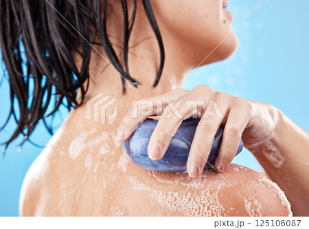 Hand, soap and shower with a woman cleaning her shoulder in studio on a blue background for hygiene. Water, bathroom and skincare with a female washing her skin for wellness or luxury treatment 125106087