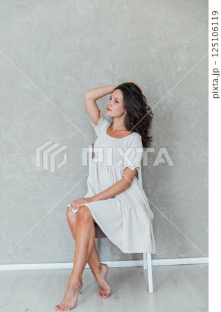 Portrait of a beautiful brunette woman in a light summer dress on a light background 125106119