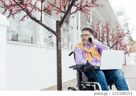 Man in a wheelchair working with a laptop negotiating on the phone 125106151