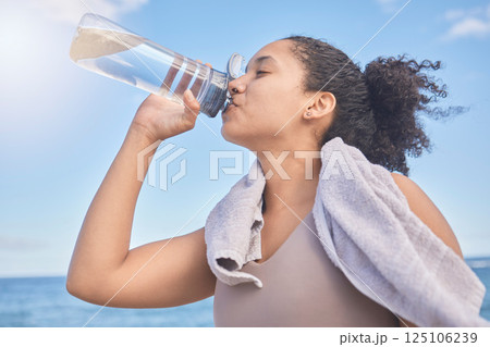 Water, fitness and woman with a drink after exercise, workout or training by the sea. Sports, motivation and energy from a runner with a bottle for hydration after running by the beach in nature 125106239