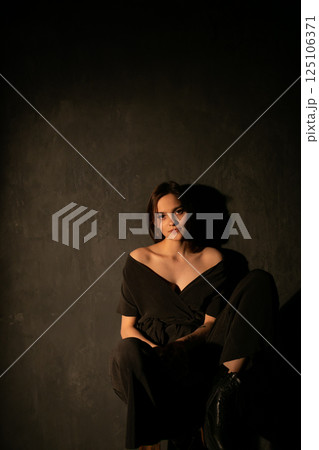 Beautiful woman in dark dress sitting on chair Beautiful woman in dark dress sitting on chair 125106371