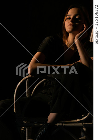 Beautiful woman in dark dress sitting on chair 125106372