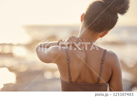 Woman, back or neck pain in nature fitness, beach workout or sunset training and anatomy crisis, muscle stress or burnout. Runner, sports athlete or shoulder injury in sunrise exercise by ocean sea Woman, back or neck pain in nature fitness, beach workout or sunset training and anatomy crisis, muscle stress or burnout. Runner, sports athlete or shoulder injury in sunrise exercise by ocean sea 125107483