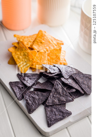 Dark and yellow nachos chips on white table. 125107559