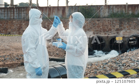 Ecologist sampling water from the river with test tube, Scientist or Biologist in a protective suit and protect mask collects sample of waste water from industrial for analyze, problem environment 125107605