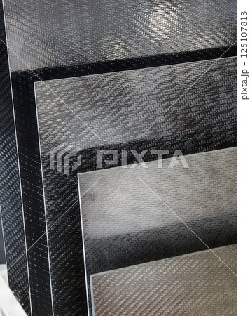 Variety of sleek carbon fiber sheets arranged in a stack showcasing different textures and colors in a workshop setting Variety of sleek carbon fiber sheets arranged in a stack showcasing different textures and colors in a workshop setting 125107813