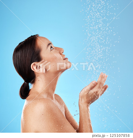 Water, shower and woman washing in a studio for body care, hygiene and to stop germs or bacteria. Health, wellness and Asian model cleaning her skin with aqua while isolated by a blue background. 125107858