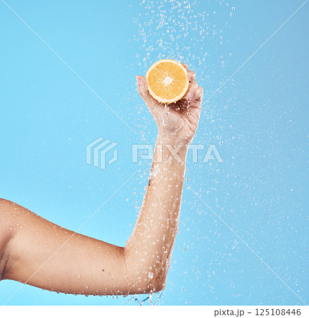 Hand, orange and water with a woman in studio on a blue background for health or hydration. Food, luxury and wellness with a female holding fruit in the bathroom shower for natural nutrition Hand, orange and water with a woman in studio on a blue background for health or hydration. Food, luxury and wellness with a female holding fruit in the bathroom shower for natural nutrition 125108446