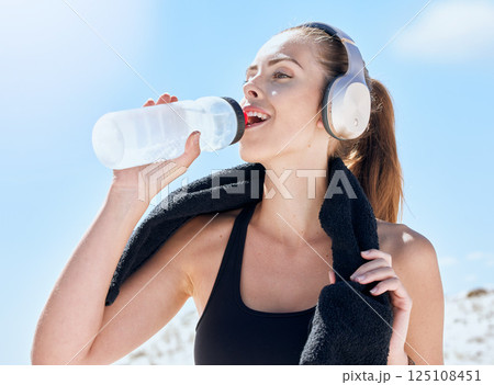 Woman, drink and water bottle during fitness, run outdoor with towel and music with headphones or streaming podcast for exercise motivation. Hydration, wellness and drinking water after workout. 125108451