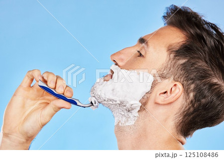 Shave, cream and man grooming his beard with a shaver in studio for health, skincare and hygiene. Foam, razor and model shaving his facial hair for a face or skin routine isolated by blue background. Shave, cream and man grooming his beard with a shaver in studio for health, skincare and hygiene. Foam, razor and model shaving his facial hair for a face or skin routine isolated by blue background. 125108486