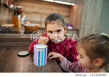 Two joyful children enjoy sweet moments in a cozy kitchen while sharing a delightful treat from a colorful container 125108989