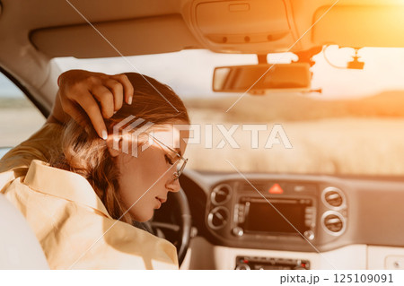 A woman in a yellow shirt is driving a car. She is wearing glasses and has her hands on the steering wheel 125109091