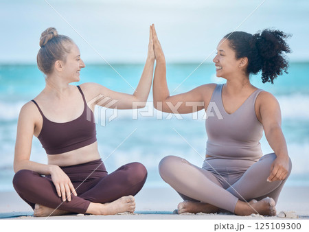 Woman, friends and high five in yoga at the beach for spiritual training or wellness exercise on the sand. Happy women relaxing touching hands in success for healthy zen or lifestyle balance together 125109300