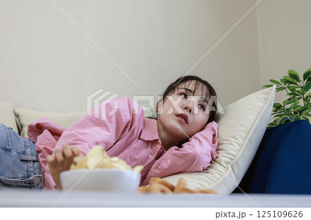 テレビを見ながらお菓子を食べる女性 テレビを見ながらお菓子を食べる女性 125109626