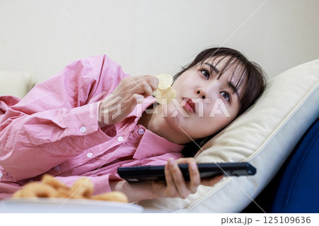 テレビを見ながらお菓子を食べる女性 テレビを見ながらお菓子を食べる女性 125109636