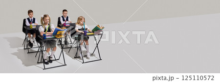 Group of children, students in school uniforms sitting at desks with books and stationery, focused on study in bright classroom. 125110572