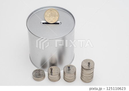 缶型の貯金箱と積み上げたコイン 125110623