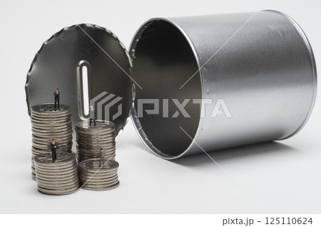 開けられた缶型の貯金箱と積み上げたコイン 125110624