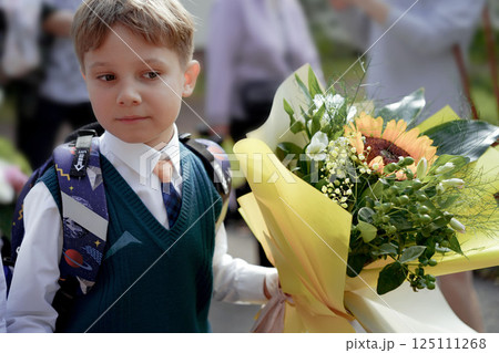 A 7-year-old boy carries a bouquet of flowers as he walks to his first day of school on September 1st, dressed in formal attire with a backpack. A 7-year-old boy carries a bouquet of flowers as he walks to his first day of school on September 1st, dressed in formal attire with a backpack. 125111268