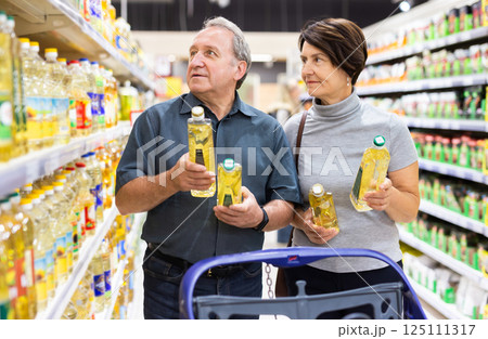 Elderly married couple choosing sunflower oil together in the grocery department of supermarket Elderly married couple choosing sunflower oil together in the grocery department of supermarket 125111317