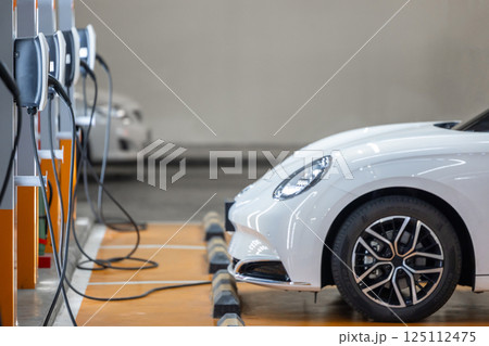 EV charging station and electric car, Electric car charging station for charge EV battery, Plug for vehicle with electric engine, EV charger clean energy, Charging point at car parking lot. EV charging station and electric car, Electric car charging station for charge EV battery, Plug for vehicle with electric engine, EV charger clean energy, Charging point at car parking lot. 125112475