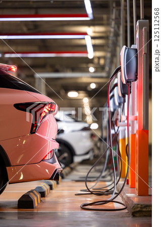 EV charging station and electric car, Electric car charging station for charge EV battery, Plug for vehicle with electric engine, EV charger clean energy, Charging point at car parking lot. 125112568