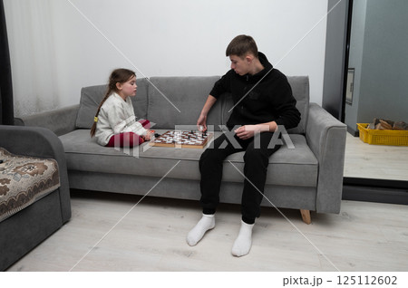 Two friends enjoying a game of checkers on a cozy gray couch in a modern living room during a peaceful afternoon 125112602