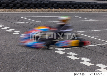 Motion blur kart driver crossing the start and finish line on kart race track circuit, Go kart racer crossing the start and finish line, Extreme sport competition winner. Motion blur kart driver crossing the start and finish line on kart race track circuit, Go kart racer crossing the start and finish line, Extreme sport competition winner. 125112742