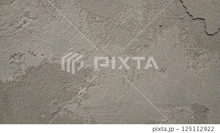 A close-up of a rough, worn-out concrete wall with a gritty texture, featuring cracks and crevices. The color is a dull, muted gray with subtle variations in shade, showing off the uneven surface. A close-up of a rough, worn-out concrete wall with a gritty texture, featuring cracks and crevices. The color is a dull, muted gray with subtle variations in shade, showing off the uneven surface. 125112922