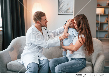 Using stethoscope. Male doctor is taking care of woman's newborn baby indoors 125113042