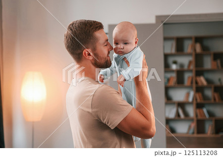 Holding kid in hands. Father with his newborn baby is indoors. Conception of single dad 125113208