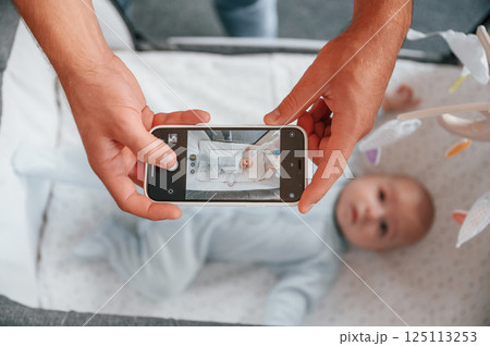 Taking picture by smartphone. Father with his newborn baby is indoors. Conception of single dad Taking picture by smartphone. Father with his newborn baby is indoors. Conception of single dad 125113253